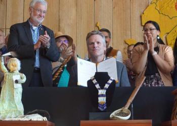 Sen. Gary Stevens and Rep. Tiffany Zulkosky, sponsors of legislation on tribal education and on state recognition of tribes, hold up the bills signed by Gov. Mike Dunleavy at a July 28 ceremony at the Alaska Native Heritage Center. The ceremony attracted a large crowd, including Native leader Emil Notti and Sen. Lyman Hoffman, standing on the stage with Stevens and Zulkosky. (Photo by Yereth Rosen/Alaska Beacon)